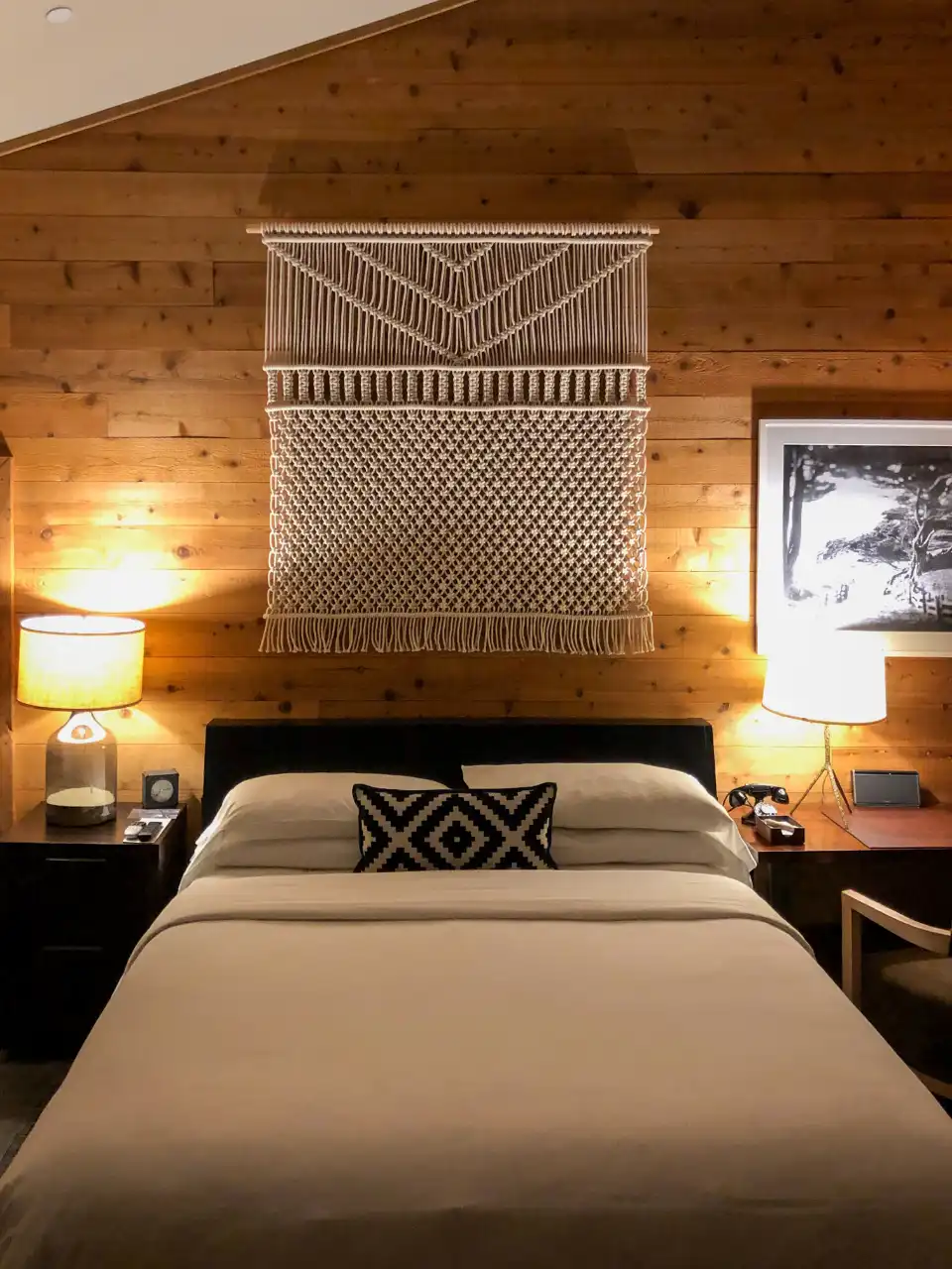 Suíte com cama de casal, parede de madeira e abajures acesos
